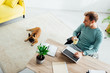 © LIGHTFIELD STUDIOS - Smiling disabled man with laptop and cup looking on french bulldog in living room
