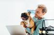 © LIGHTFIELD STUDIOS - Smiling man holding french bulldog while working on laptop