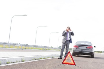 Wall Mural - Stressed businessman talking on smartphone and asking help for his broken car