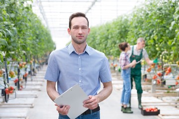 Confident supervisor standing against farmers in Greenhouse