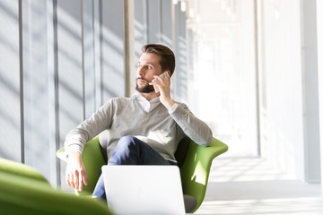 Wall Mural - Businessman talking on smartphone while sitting and waiting in office lobby