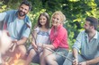 © MDBPIXS - Tilt shot of smiling family with male friend roasting sausages over campfire at park