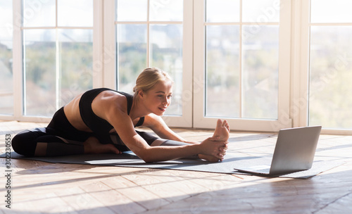 Cuadros en Lienzo Flexible girl doing yoga at home, looking at laptop screen