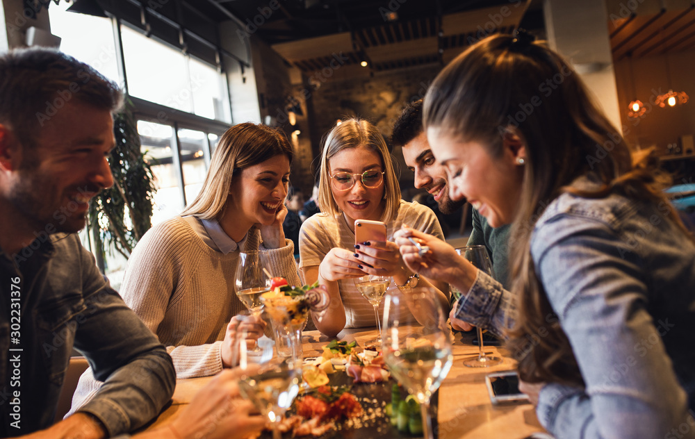 Group of young friends having fun in restaurant, talking and laughing while dining at table. - obrazy, fototapety, plakaty 