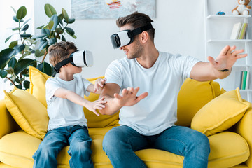 Poster - happy father and son in virtual reality headsets gesturing in living room