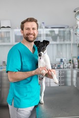 Wall Mural - Smiling Veterinarian holding dog in clinic