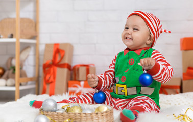 Wall Mural - Playful baby elf helping to decorate Christmas tree with balls