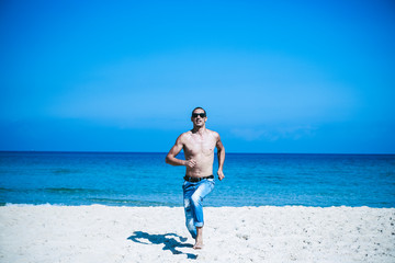 young muscular man resting and posing on the beach. Run towards us