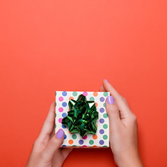 Wall Mural - Woman manicured hands holding green gift box on dark orange background, copy space, top view, flat lay. Giving presents or shopping concept. Background for holidays