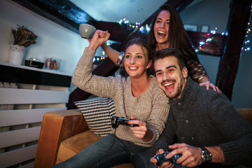 Group of best friends sitting at home on pleasant evening and playing games on console.They challenge each other to win .	