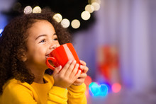 Cute Little African Girl With Cup Of Hot Cocoa Near Christmas Tree