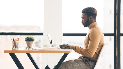 Poster - Afro businessman working on laptop in modern office, side view