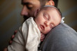 © Cavan Images - Close up of newborn baby's face sleeping on father's shoulder at home