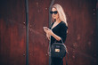 © Nomad Pixel - Image of beautiful business woman holding mobile phone. Young woman standing at the street and using mobile phone.Woman listening to music with the phone
