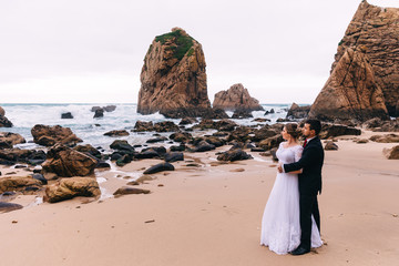 bride and groom embraced each other near the ocean on the backgr