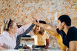 © Westend61 - Happy young people sitting together at table high fiving