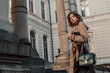 © Victoria Fox - Outdoor autumn fashion portrait of young elegant woman wearing beige black trench coat, beret, holding green faux leather textured crocodile bag, posing in street of European city. Copy, empty space
