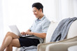 © Blue Jean Images - Happy young Chinese man using laptop in living room