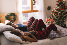 Two Fun Beautiful Friends Smiling Each Other In Bed At Home Near Christmas Tree In Cozy Interior. Interior With Christmas Decorations.