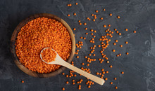 Red Raw Organic Bio Lentils In A Wooden Bowl With A Wooden Spoon Stuck In It On A Dark Background. Place For Text