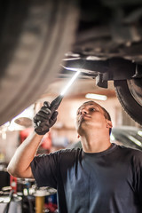 Wall Mural - Auto mechanic repairer checking condition under car on vehicle lift