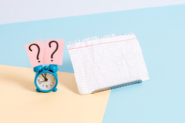 Mini size alarm clock beside a Paper sheet placed tilted on pastel backdrop