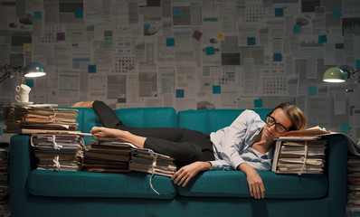 Stressed businesswoman sleeping on a couch with lots of paperwork