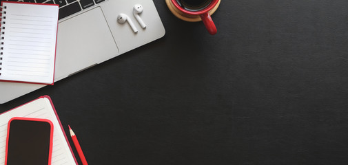 Top view of dark modern workplace with notebook, laptop computer and office supplies on black table