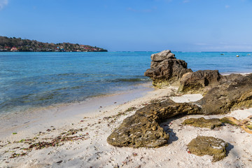 Wall Mural - Weathered rocks on white sand beach, Nusa lembongan, Bali, Indonesia. Clear blue ocean with boats beyond. Neighboring island of Nusa Penida in the distance. 