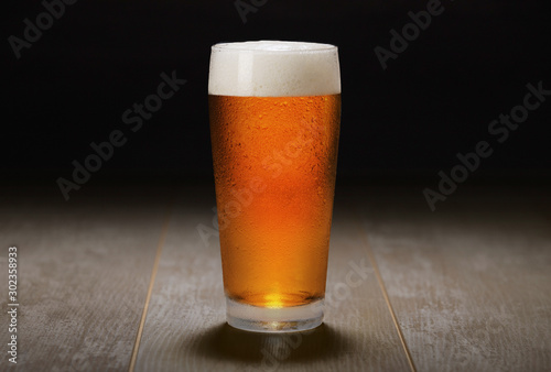 Double India pale ale beer served in a chilled pint glass on wooden counter at a craft beer pub, black background