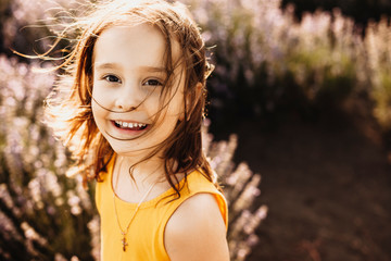 Portrait of a lovely little girl looking at camera laughing while being in a field of flowers against sunset dressed in yellow.