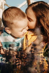 Wall Mural - portrait of a lovely little girl kissing with closed eyes and embracing her little brother outdor in