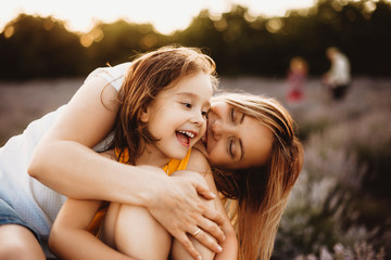 Wall Mural - beautiful little girl laughing while being embracing by her young mother outdoor in field of flowers