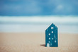 © tonktiti - Small home model on sand beach with blue sky background.