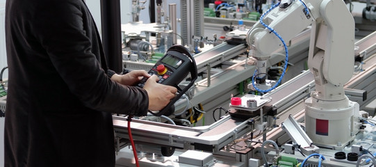 industry 4.0 concept: Man (engineer) is programming robotic arm with control panel (teach pendant) on smart factory production line background. Selective Focus.