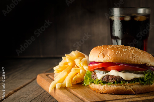 Home made hamburger with beef, onion, tomato, lettuce and cheese. Fresh burger close up on wooden rustic table with potato fries, beer and chips. Cheeseburger. © xander21