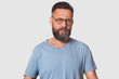 © sementsova321 - Close up portrait of angry man posing in studio isolated over white wall, guy wearing spectacles and gray casual t shirt, having beard, sytanding with anger facial expression. People emotions concept.