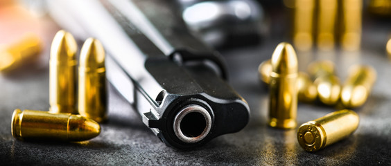 Hand gun detail with ammunition on stone table banner or panorama photo. 9 mm pistol gun weapon and bullets at dark background.