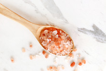 Top View Of Himalayan Pink Salt In Wooden Spoon On White Marble Table.