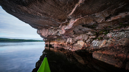 Wall Mural - Green canoe on a lake under cliffs