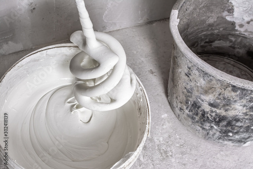 Fotomural Plastic bucket with fresh putty, spiral whisk for electric building mixer soiled with putty and empty dirty bucket on raw concrete floor