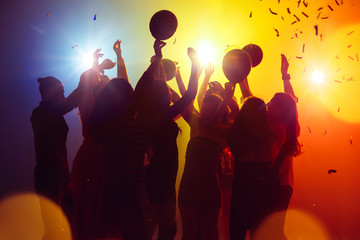 Balloons. A crowd of people in silhouette raises their hands on dancefloor on neon light background. Night life, club, music, dance, motion, youth. Yellow-blue colors and moving girls and boys.