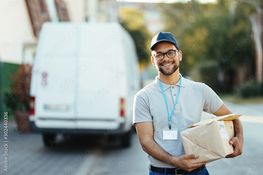 Portrait of young happy courier with packages for a delivery. - obrazy, fototapety, plakaty 