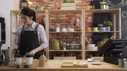 Wall Mural - beautiful asian japanese bartender girl preparing black coffee pour in white cup and putting on wooden tray on counter table in cafe store. elegant female barista making customer order in coffeehouse