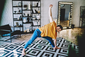 Fototapete - Young man doing sportive exercises during stretching training on carpet at home interior.Motivated hipster guy leads healthy lifestyle and maintains a vital tone in modern apartment