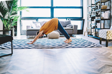 Fototapete - Motivated young man standing in yoga pose on carpet in modern apartment with stylish interior.Hipster guy in sportive wear leads healthy lifestyle during morning sportive exercises at home