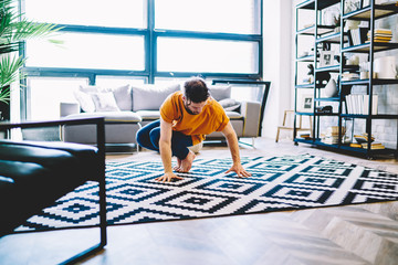 Fototapete - Young man dressed in active wear doing yoga exercises during morning training at home interior.Hipster guy practising relaxation during sportive training in modern apartment