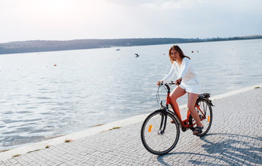 Wall Mural - Cheerful girl rides bike on the beach near the lake at sunny daytime