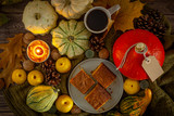 Fototapeta Kuchnia - Cisto z dyni na jasnym talerzu, obok znajdują się dynie, pigwa, szyszki, liście, orzechy, kawa i świeczka
