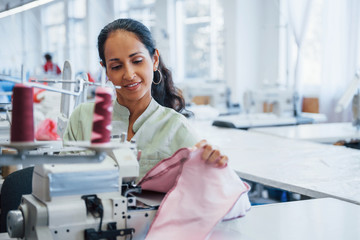 Dressmaker woman sews clothes on sewing machine in factory